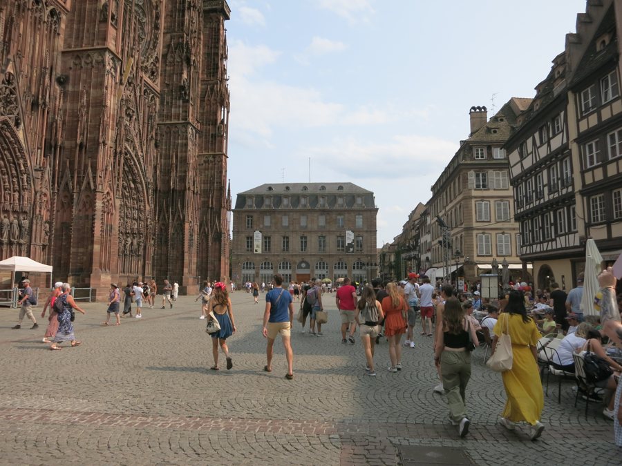 Besucher auf dem gepflasterten Münsterplatz in Straßburg vor der Kathedrale und Fachwerkhäusern.